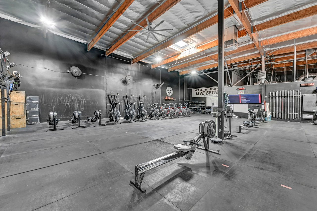 Commercial gym with rows of rowing machines and bikes beneath exposed timber beams.