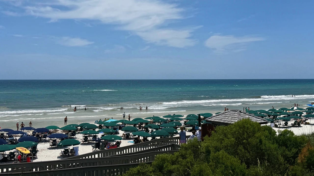A busy summer day at Rosemary Beach with green umbrellas, beach chairs, and people swimming in the emerald water.