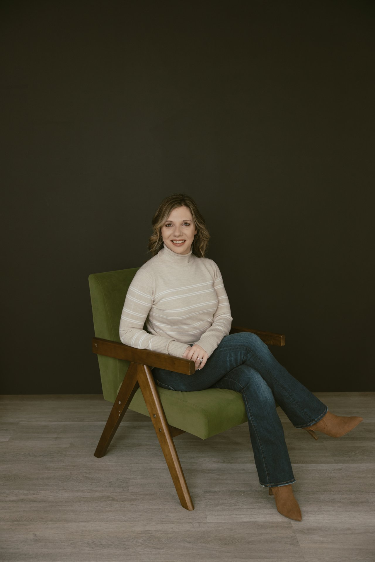 Kendayle Helmberger seated in a green chair, wearing a light striped sweater and jeans.