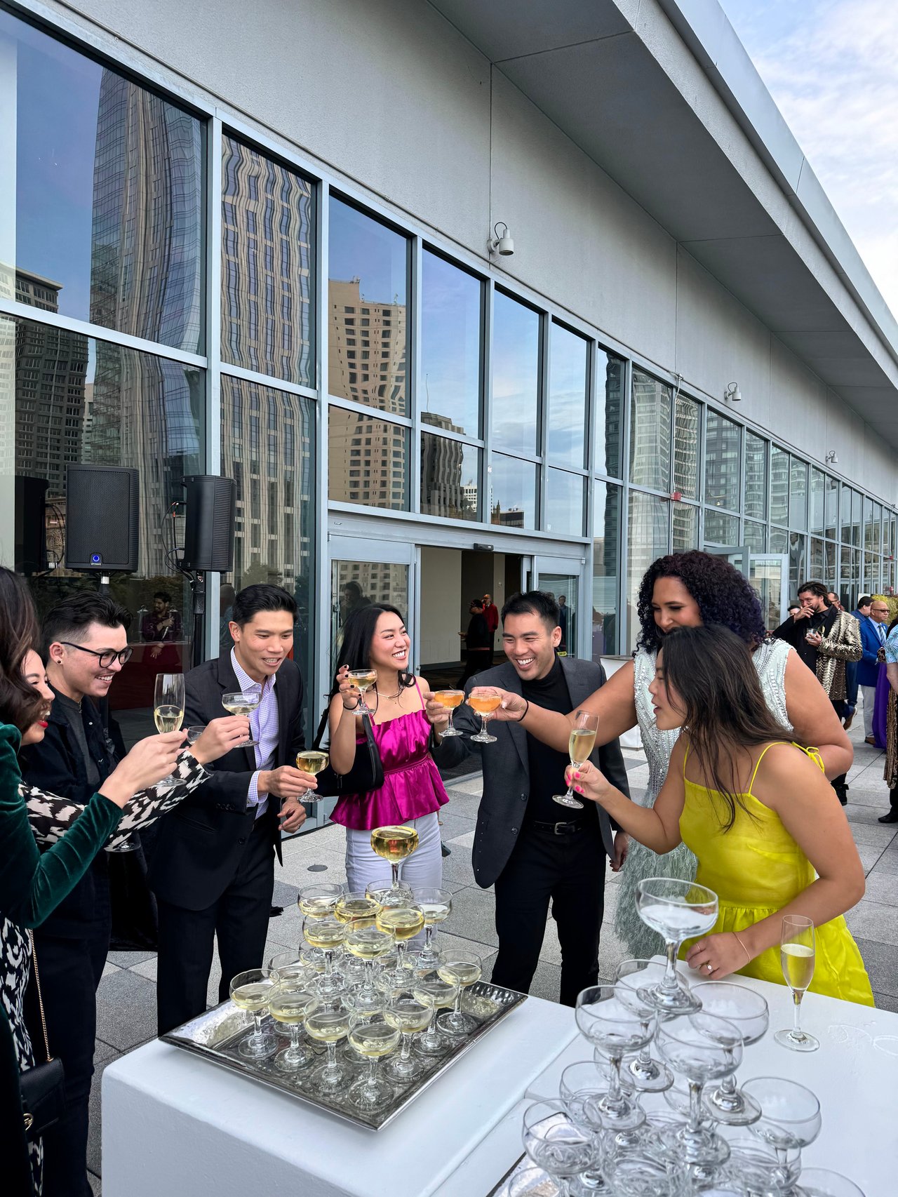 Real estate professionals toast at an outdoor gathering beside a glass-fronted building.