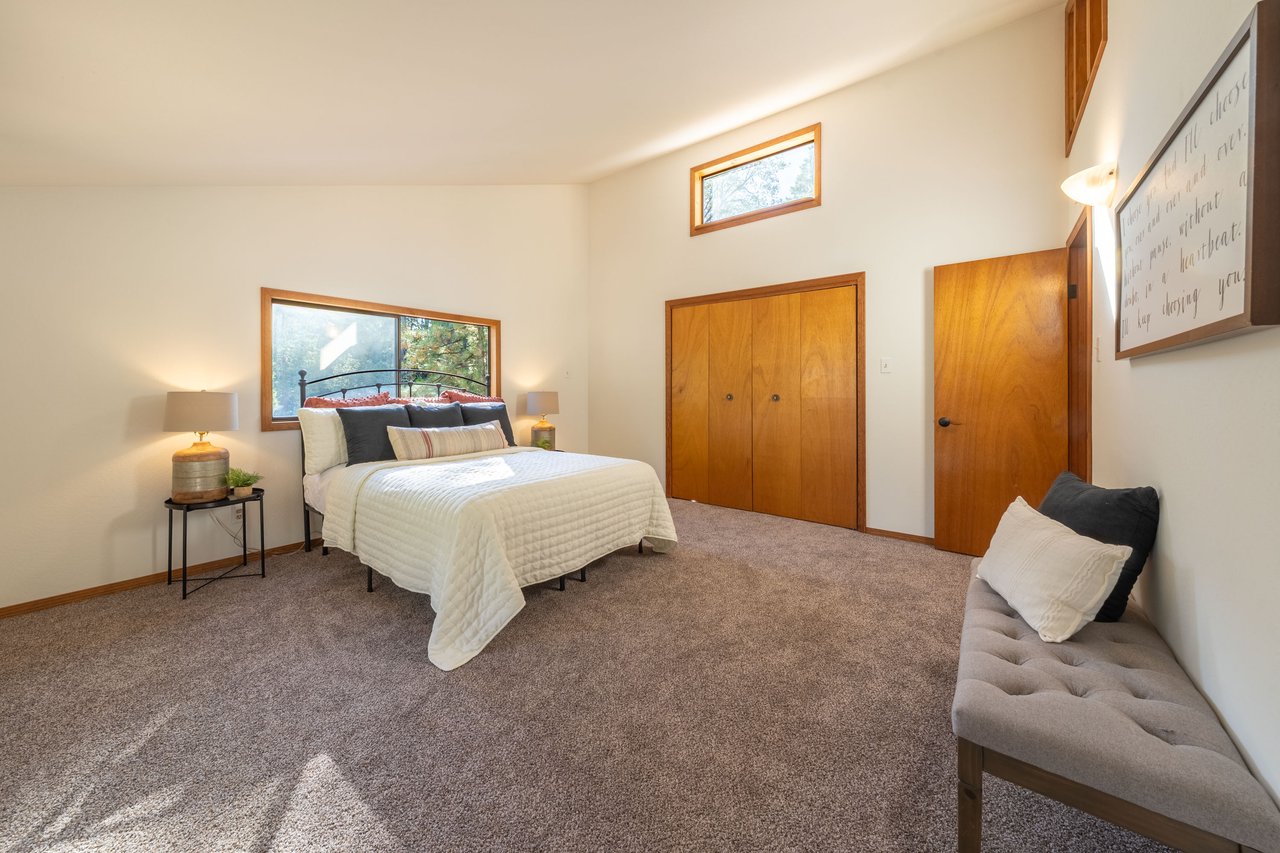 Furnished bedroom with a king-size bed, warm wood closet doors, and a gray loveseat.