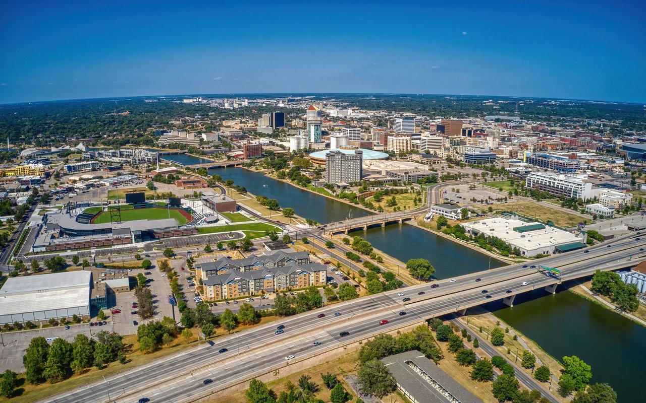 Aerial city panorama with a river, downtown buildings, baseball stadium, and highway.