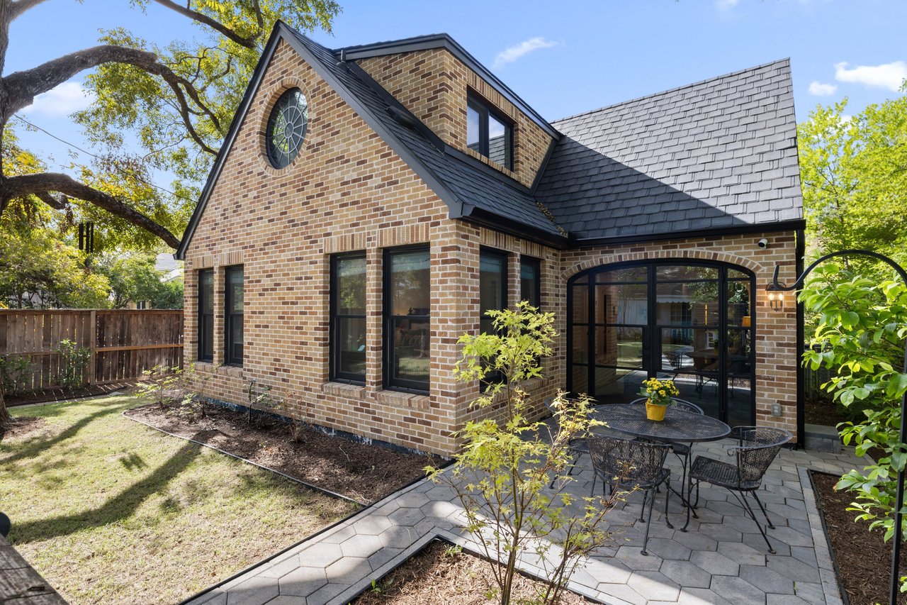 Brick house with a round gable window and a paved patio furnished with outdoor dining furniture.
