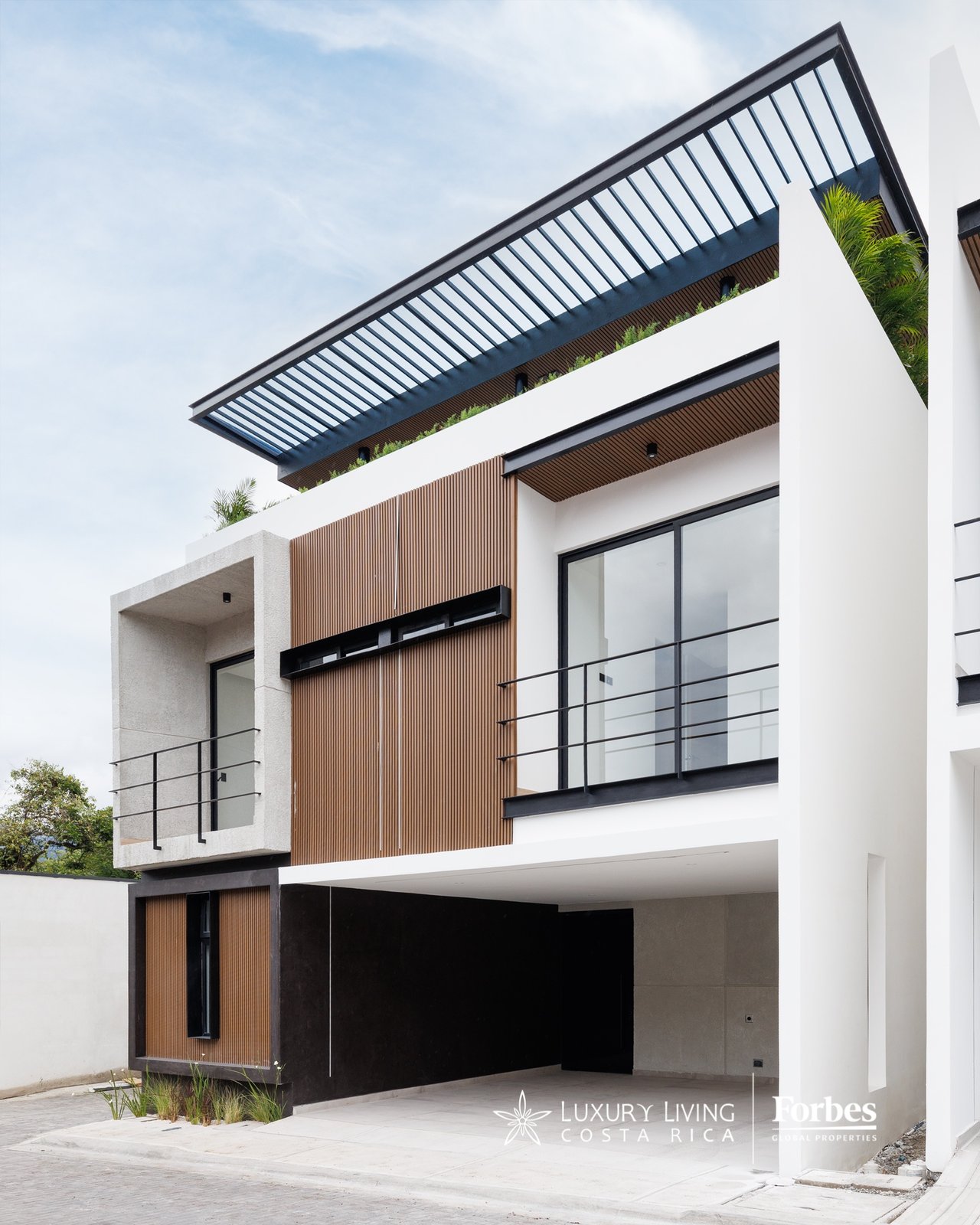 Modern white home with wood-slat facade, rooftop pergola, glass balcony, and covered carport.