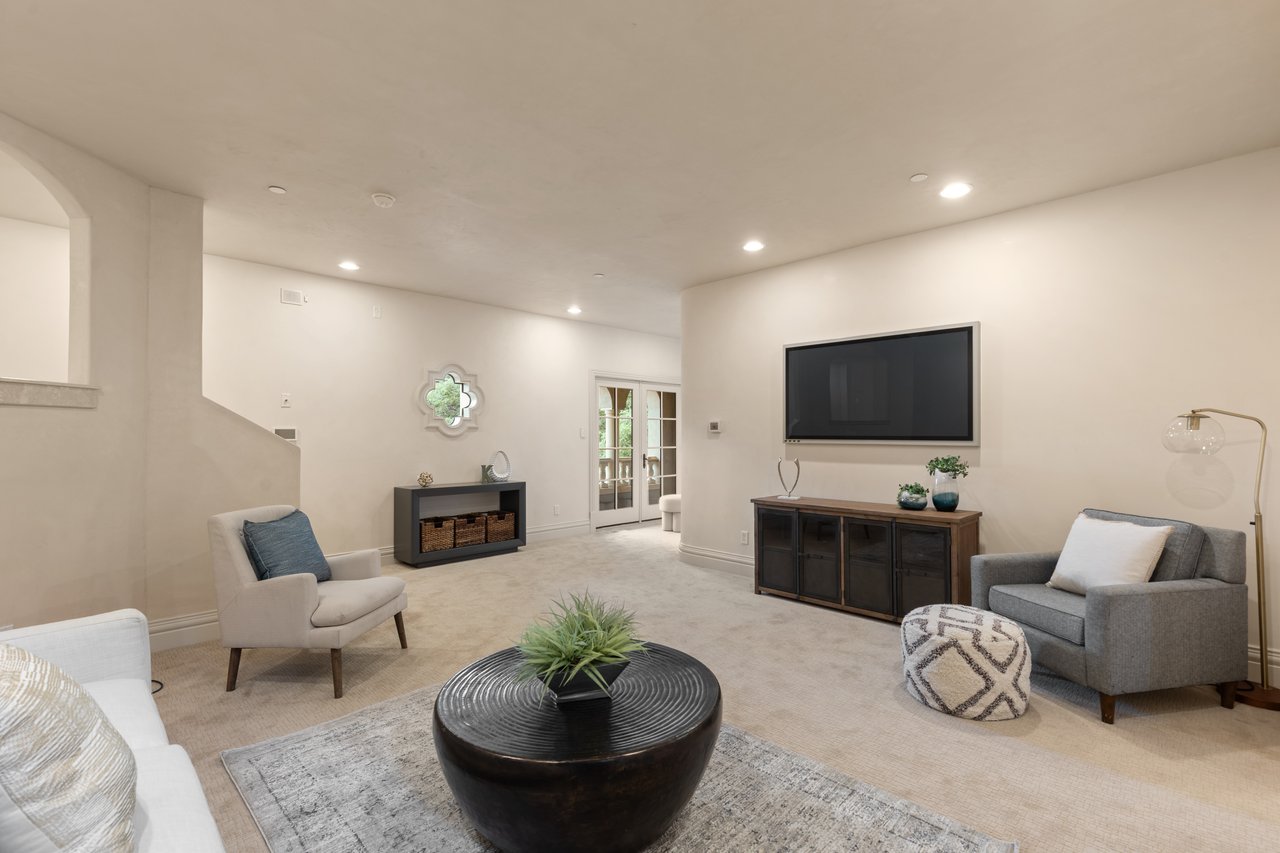 Staged living room with a wall-mounted television, French doors, and a round coffee table with a plant.