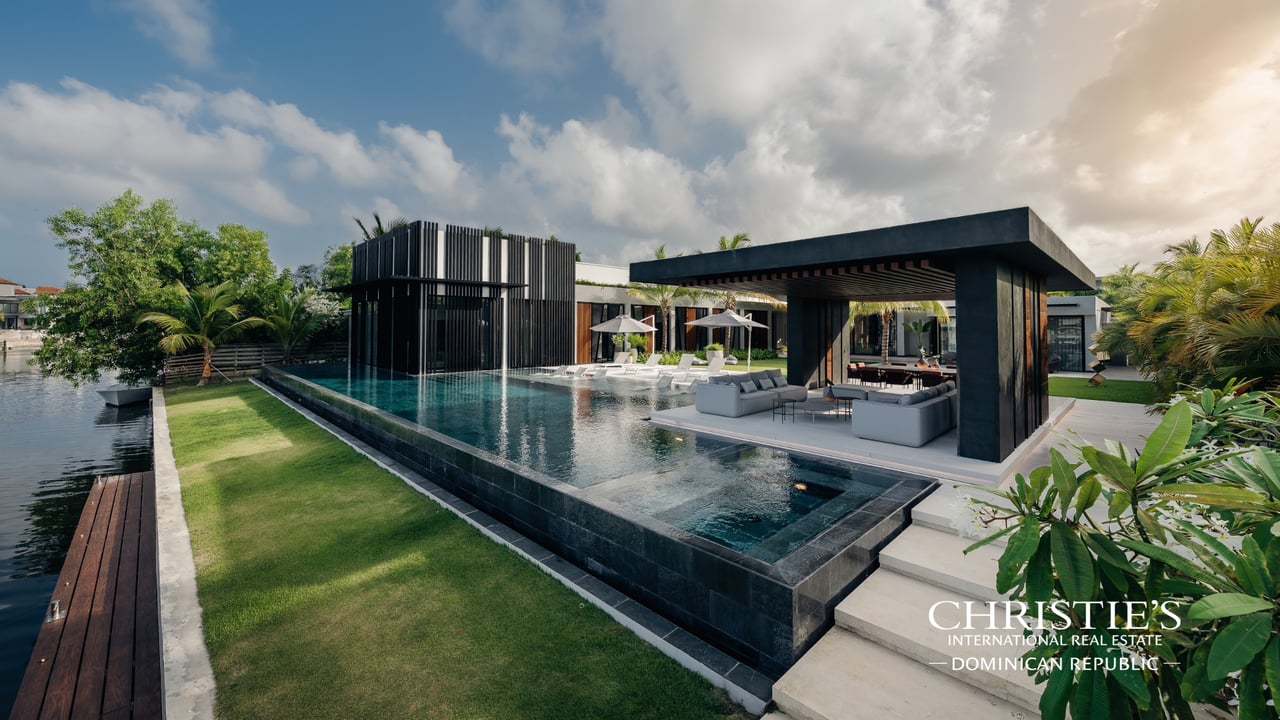 Modern waterfront villa with an infinity pool, covered lounge, and canal-side lawn.