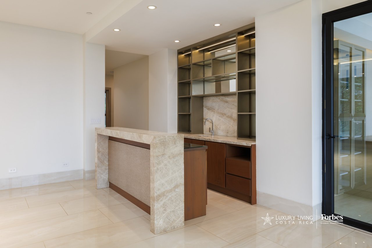 Built-in apartment bar with illuminated shelving, a small sink, and a stone peninsula.