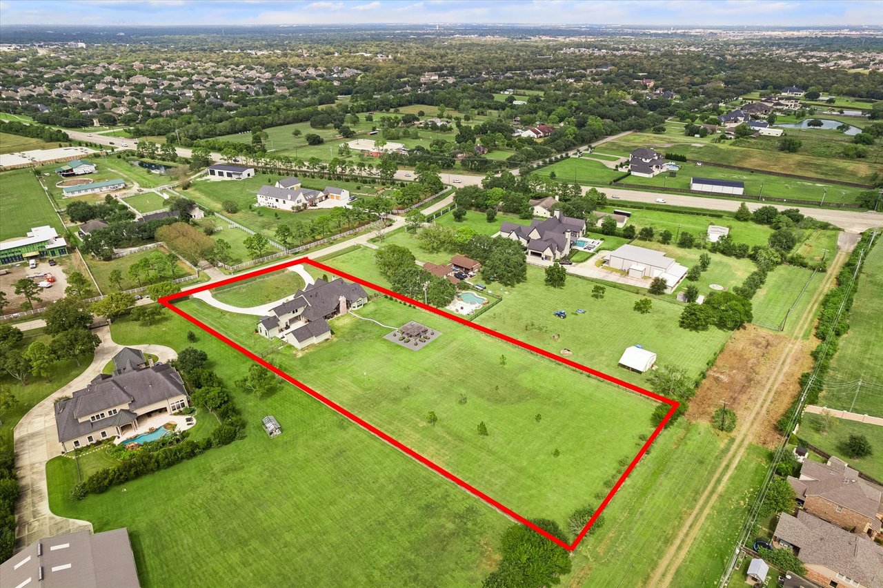 Aerial view of a large grassy property outlined in red, with a house and curved driveway.