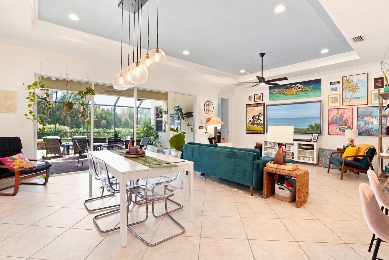 Open living and dining room with a teal sofa, glass doors, and a tropical outdoor dining area.