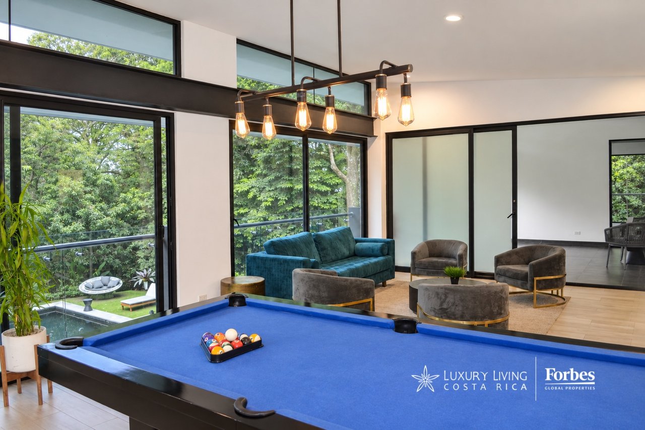 Apartment game room with a blue pool table, lounge seating, and large windows overlooking greenery.