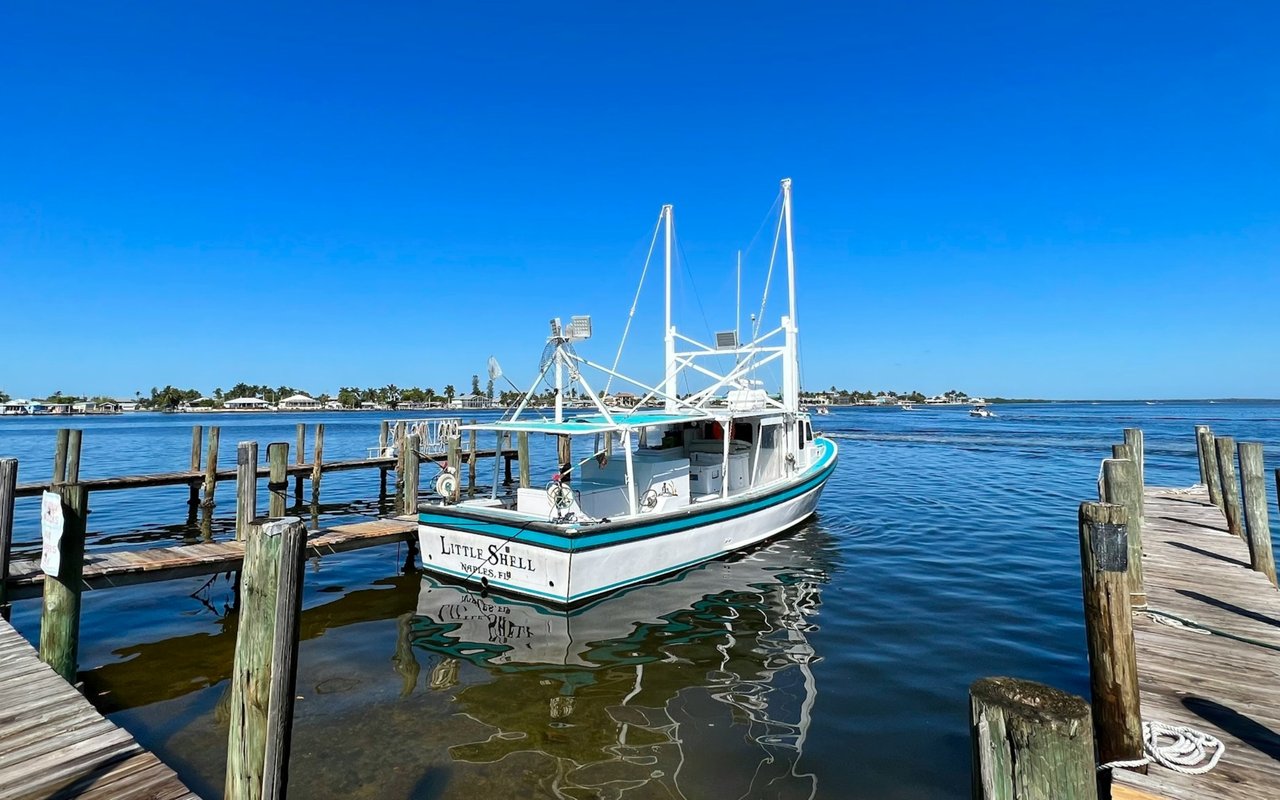 Fishing boat moored between wooden docks, with homes and palm trees along the far shore.