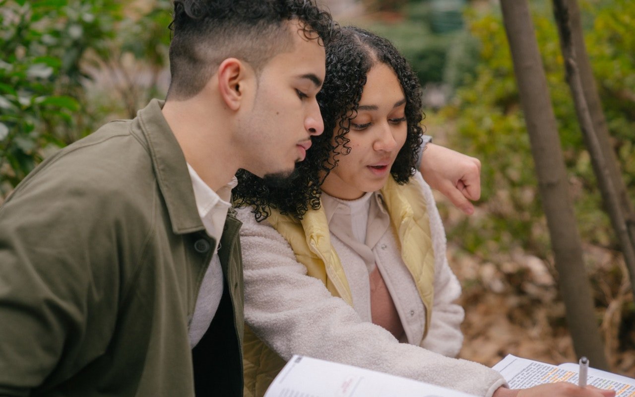 Two young adults outdoors look over a document together.