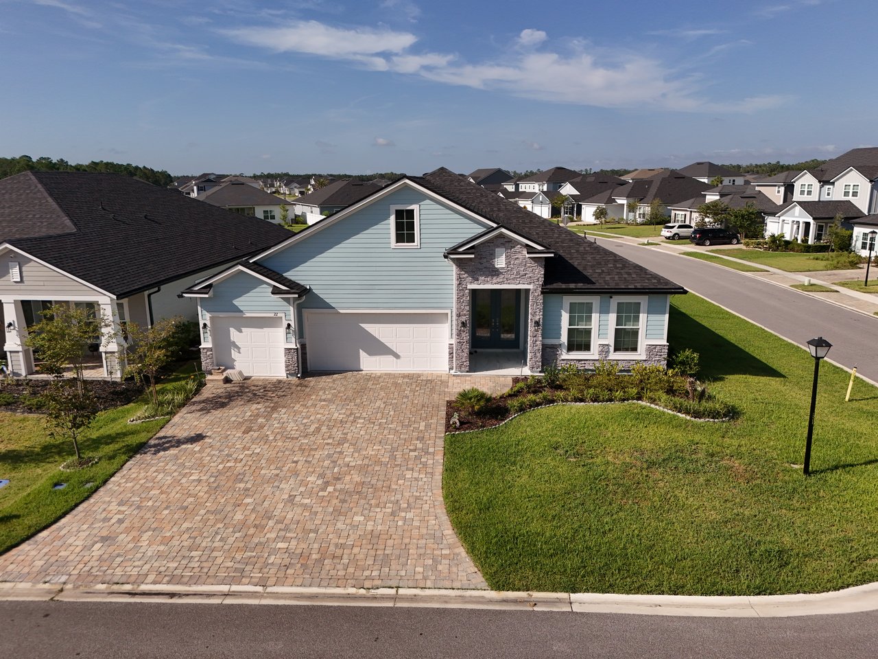 Light blue single-story home with stone entry accents, a wide paver driveway, and landscaped lawn.