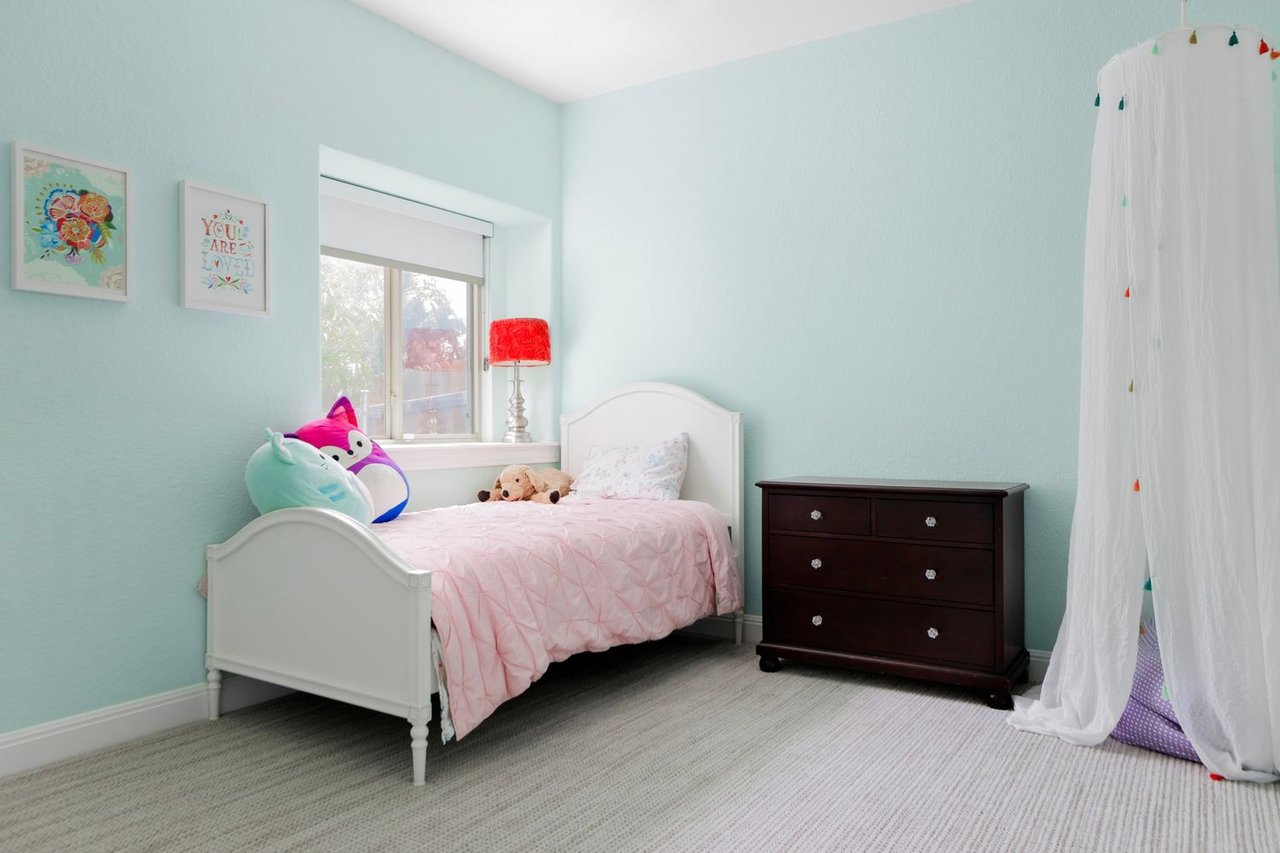 Bedroom with pale aqua walls, a pink-covered white bed, and a dark wood dresser.
