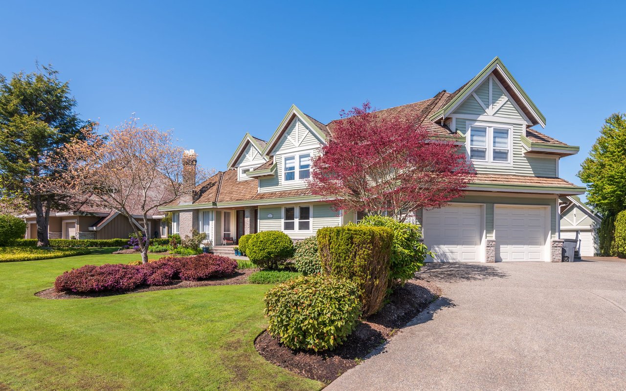 Large two-story house with green siding, white trim, peaked dormers, and a curved driveway.