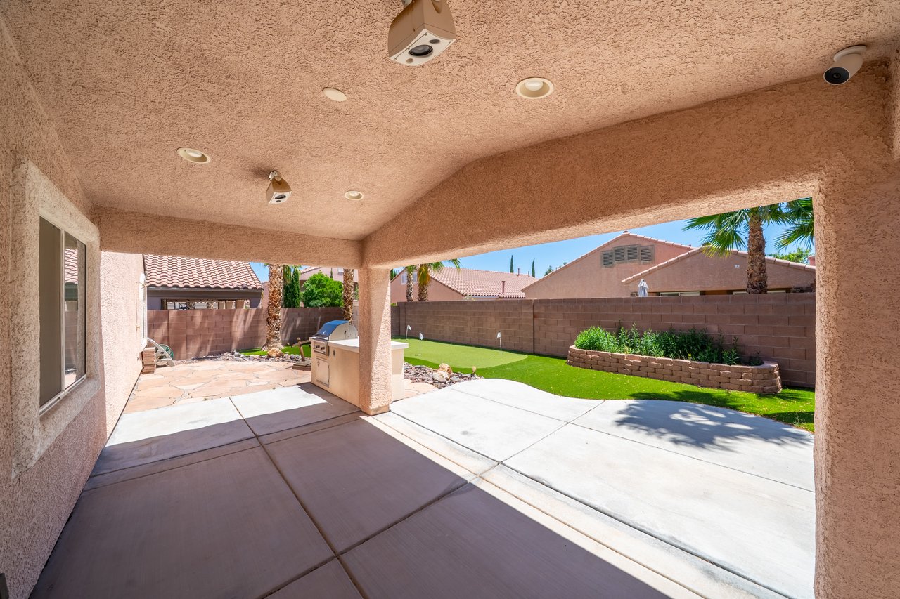Covered backyard patio with an outdoor grill, artificial turf, and a raised planter bed.