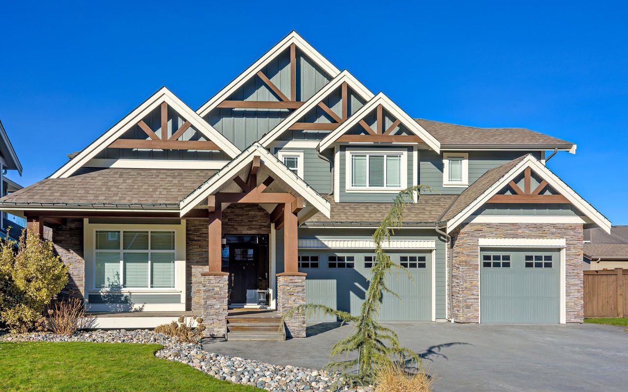 Two-story gray-green home with stone accents, prominent gables, and a timber-framed entrance.