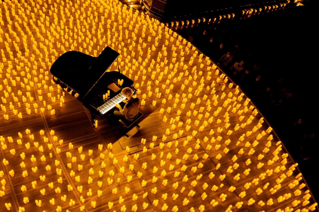 Pianist performs on a grand piano surrounded by rows of glowing candles.