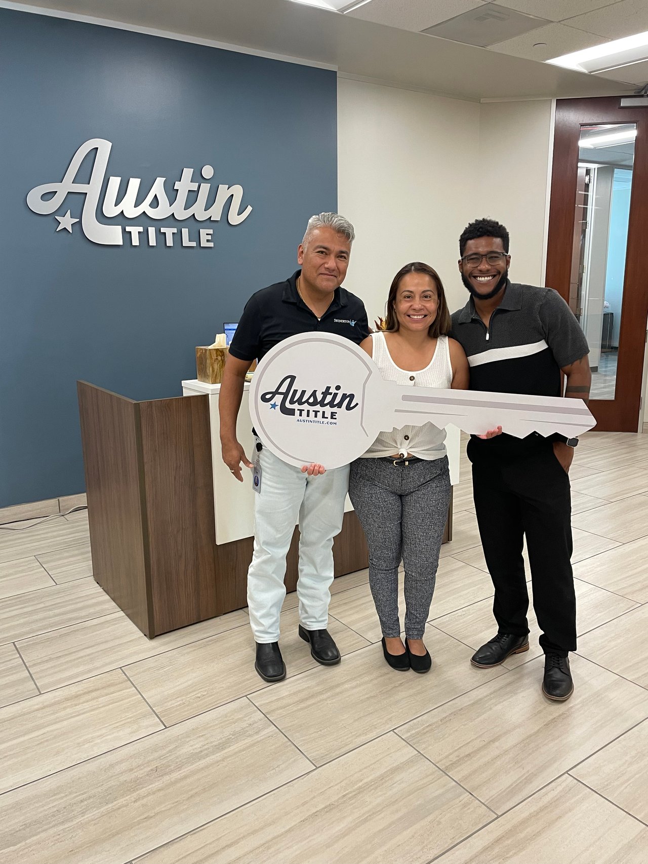 Three adults pose with a large Austin Title key sign inside the office.