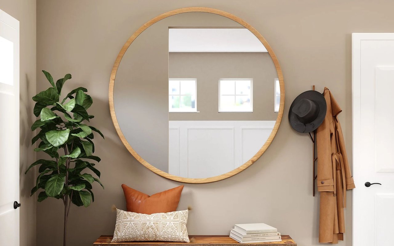 Furnished entryway with a round wood-framed mirror, bench, leafy plant, and coat rack.