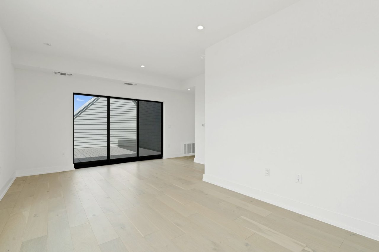 Vacant room with pale wood floors and black-framed sliding glass doors to a deck.