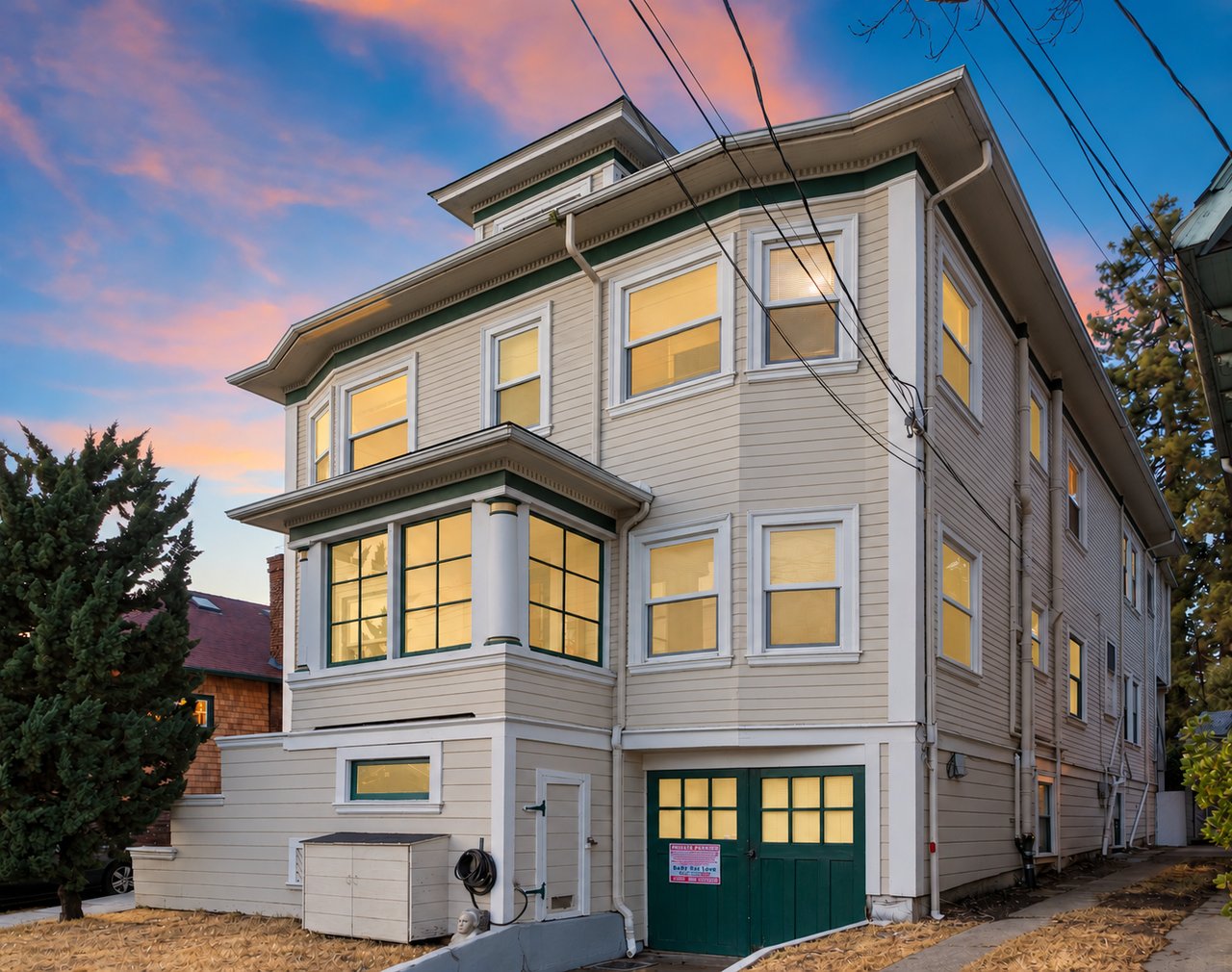 Multi-story beige building with green trim and glowing windows beneath a pink-and-blue dusk sky.