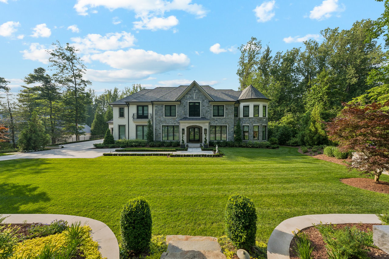 Large stone-and-white house with a turret, broad lawn, and landscaped gardens.