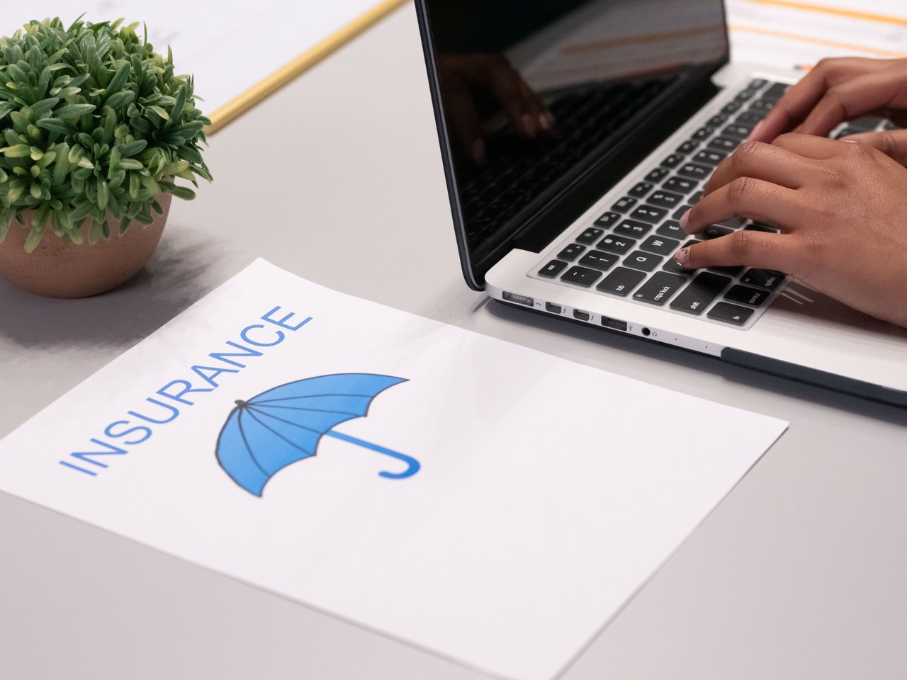 Hands typing on a laptop beside an insurance paper with a blue umbrella illustration.