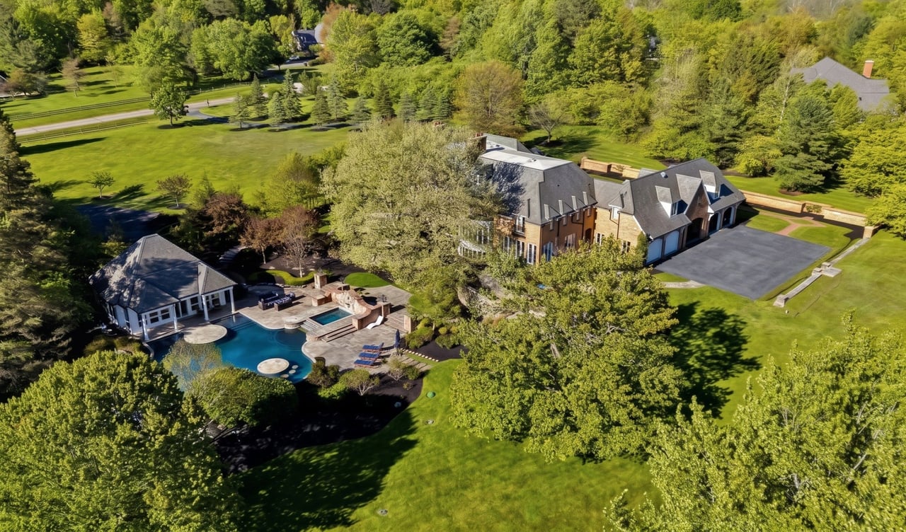 Large brick home with a swimming pool, pool house, and wooded grounds