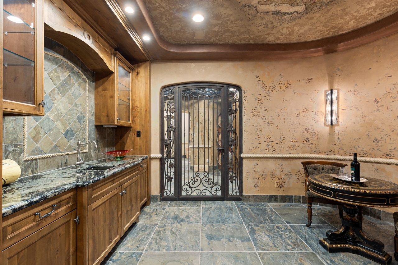 Furnished wine room with wood cabinetry, granite counter, tiled floor, and ornate iron gate.