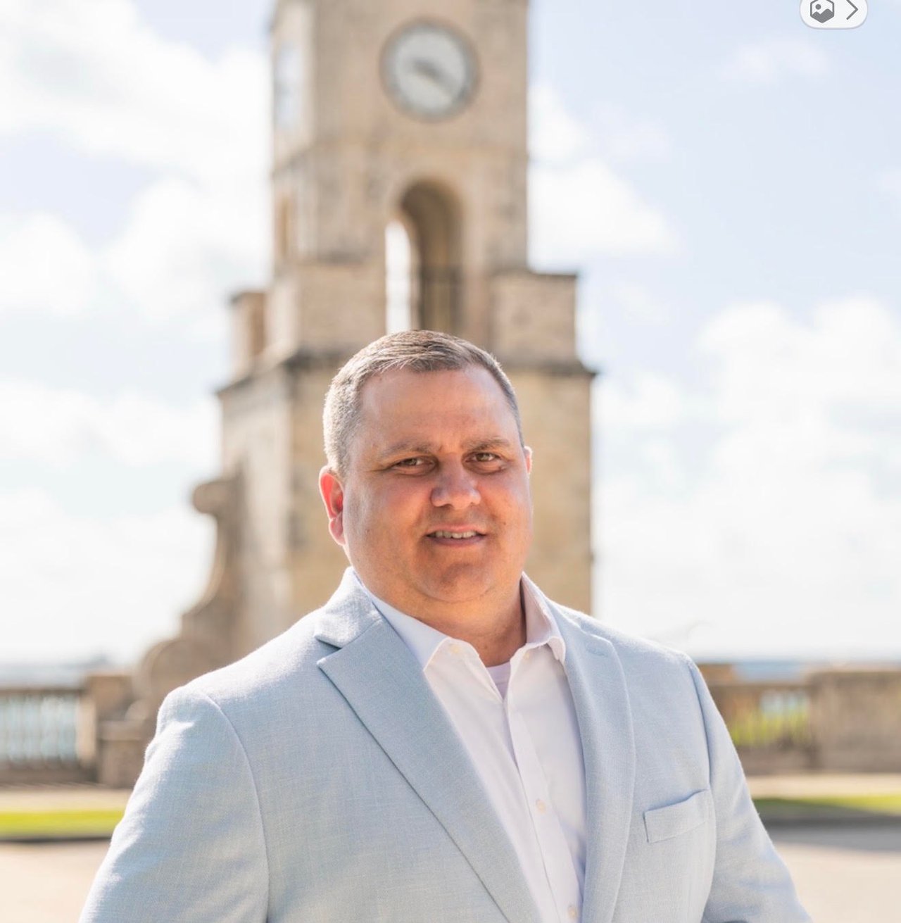Jason Jarrelle in a light blue blazer, posing in front of a stone clock tower.