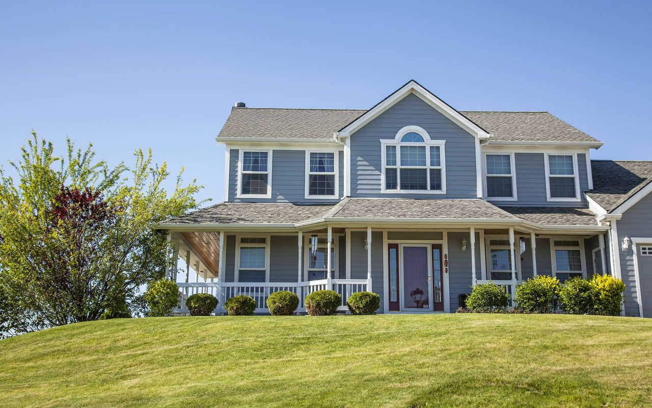 Blue-gray two-story house with white trim, a covered porch, and a broad sloping lawn.