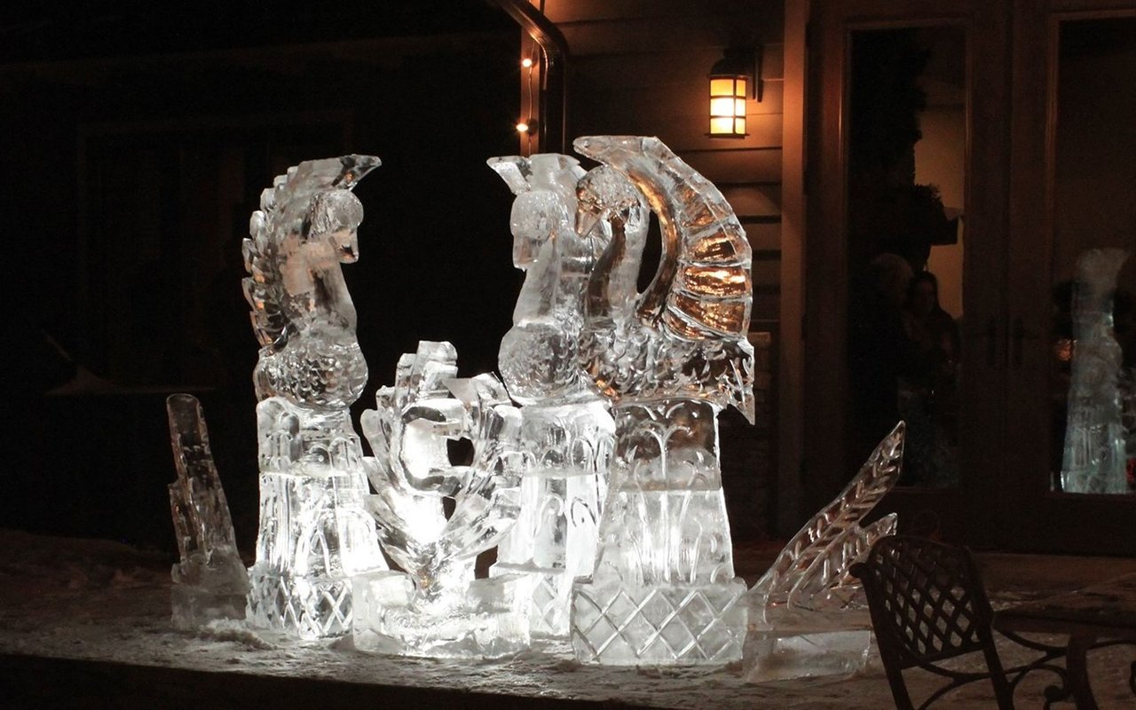 Intricate ice sculpture displayed outside a warmly lit building at night.