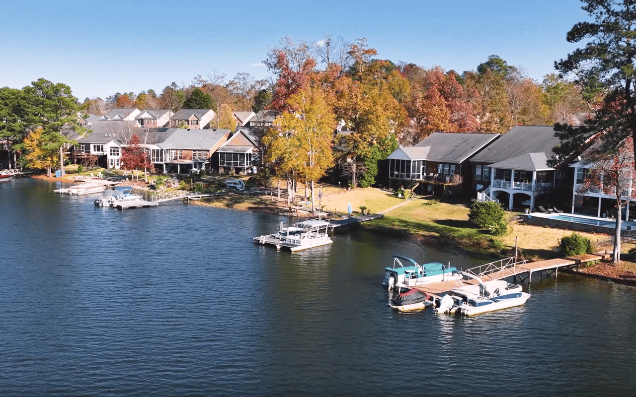 Aerial view of lakeside homes with docks and boats along an autumn-colored shore.