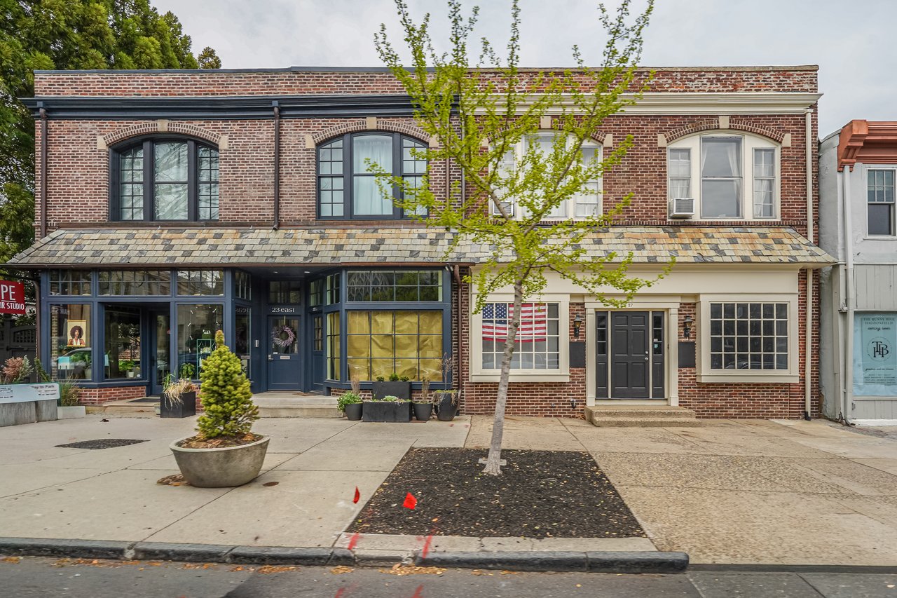 Brick row building with storefronts, arched upper windows, and a small American flag by the entrance.