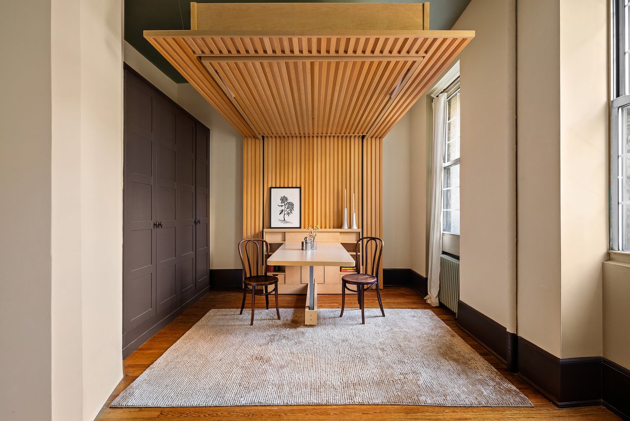 Studio dining area with a sculptural slatted wood platform overhead and dark built-in cabinets.