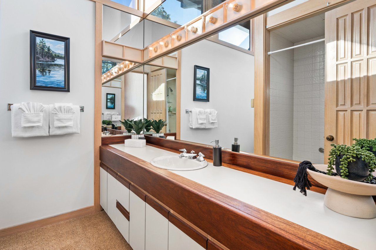 Bathroom with a long wood-trimmed vanity, large mirrors, and an open tiled shower.