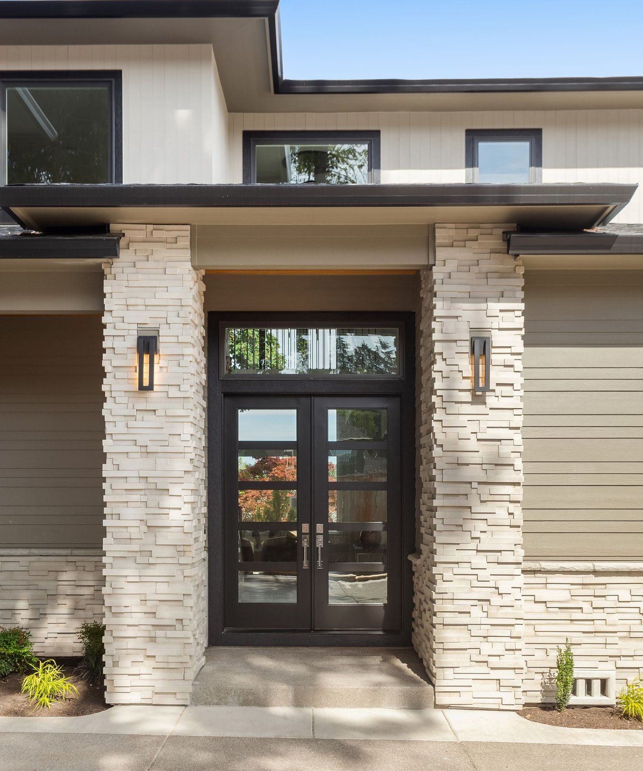 Modern home entrance with dark glass double doors and pale stacked-stone columns.