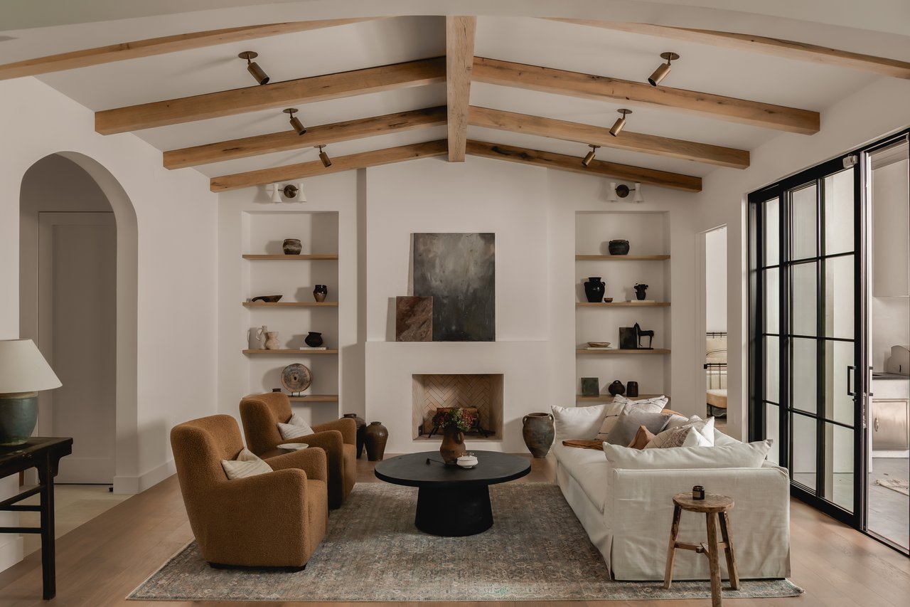 Living room with exposed wood beams, a fireplace, built-in shelves, and black-framed glass doors.