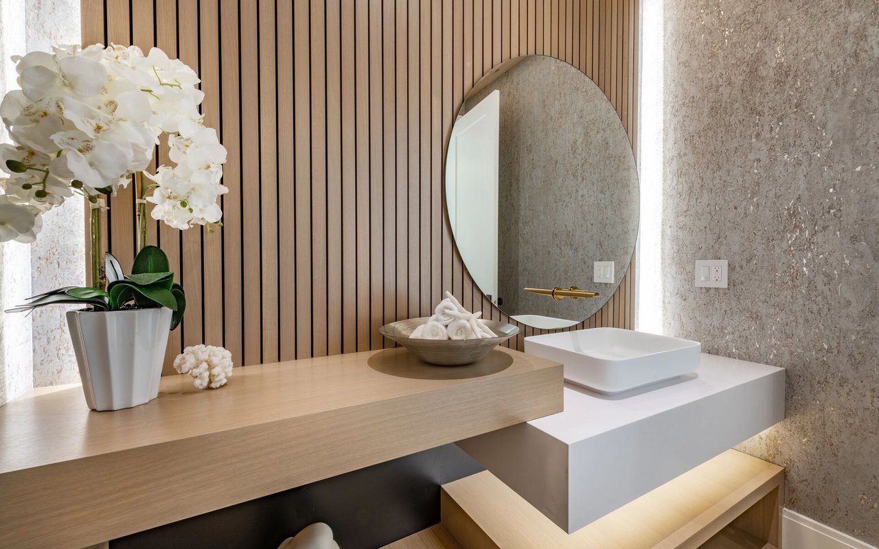 Modern bathroom vanity with a white vessel sink, oval mirror, wood slat wall, and orchids.