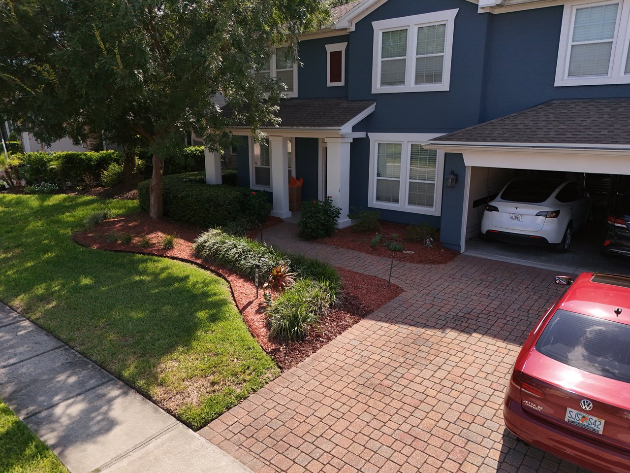 Blue two-story house with white trim, an attached garage, and a brick-paver driveway.