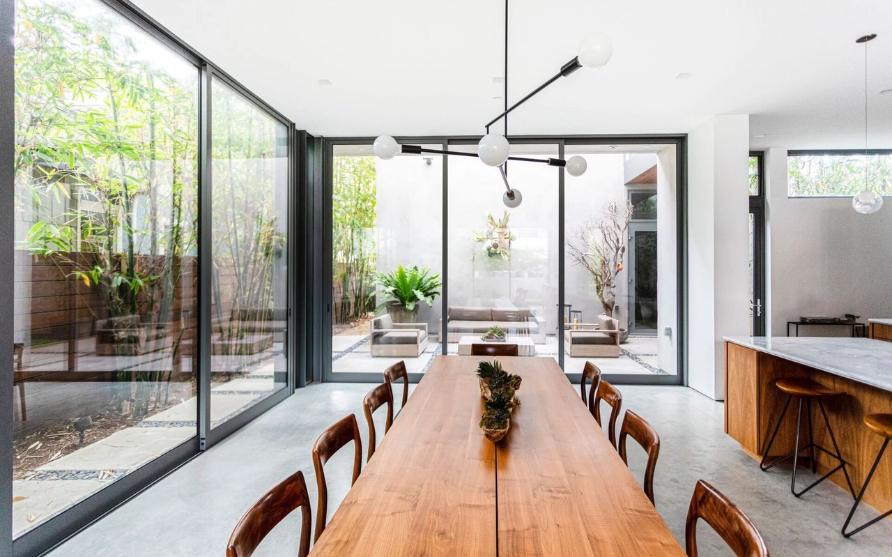 Contemporary dining room with a long wood table, sculptural chandelier, and glass walls facing a planted courtyard.