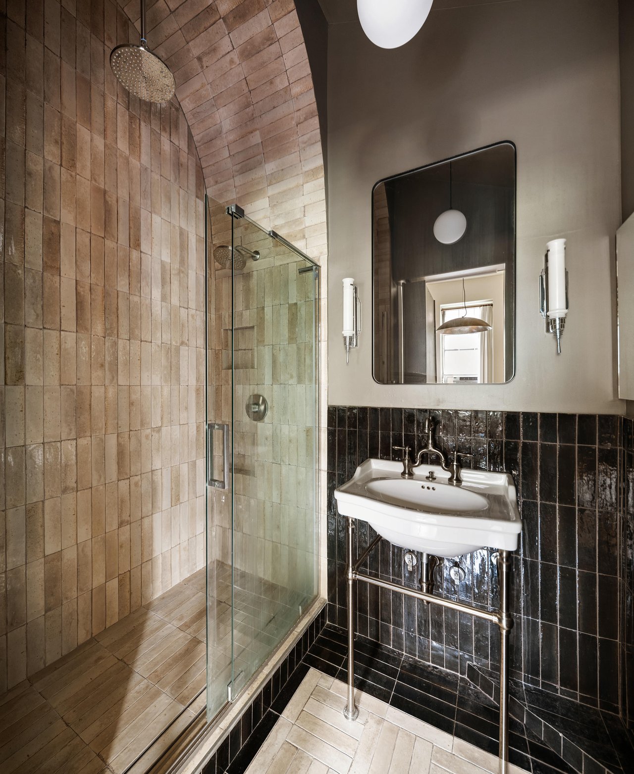 Bathroom with an arched beige-tiled shower, glass enclosure, and wall-mounted sink against dark tile.