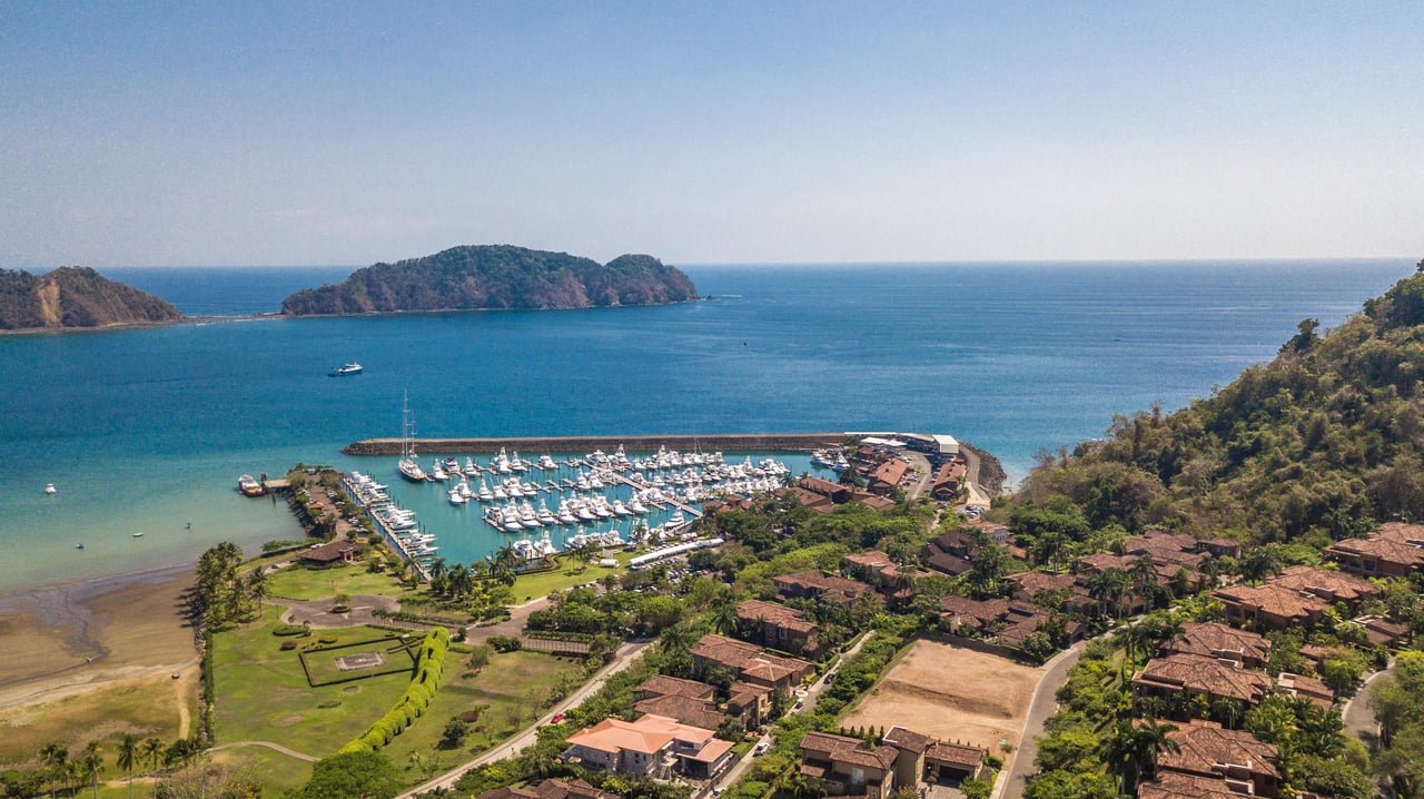 Coastal marina with boats and nearby homes, backed by blue ocean and a wooded island.