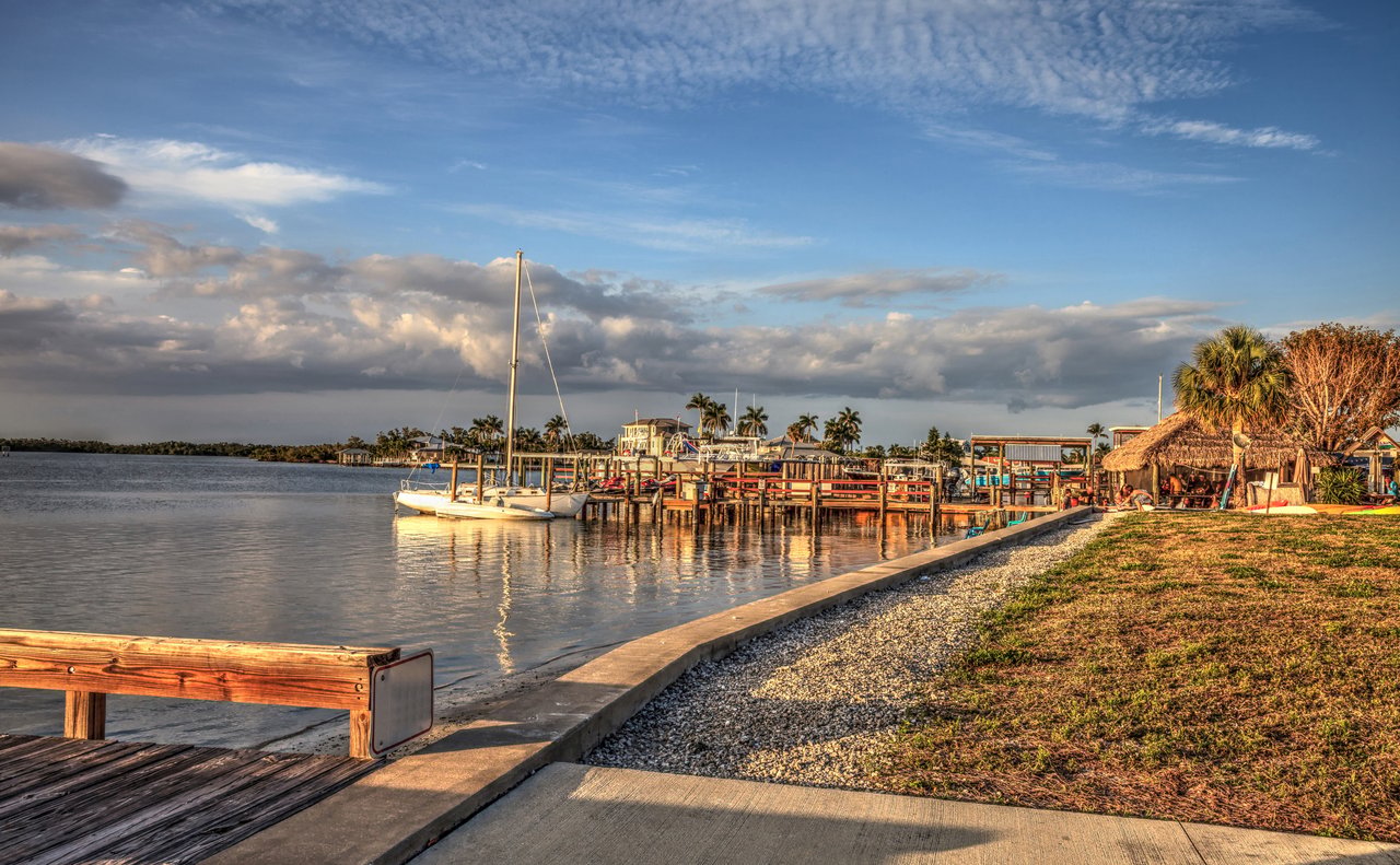 Isles of Capri waterfront marina with sailboats, docks, and a thatched-roof pavilion.
