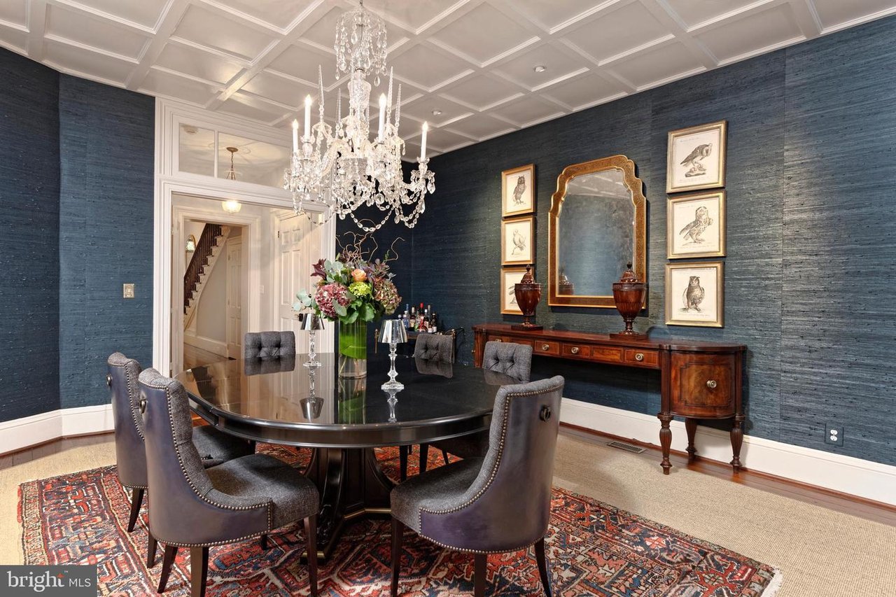 Dining room with a crystal chandelier, dark oval table, blue walls, and patterned rug.