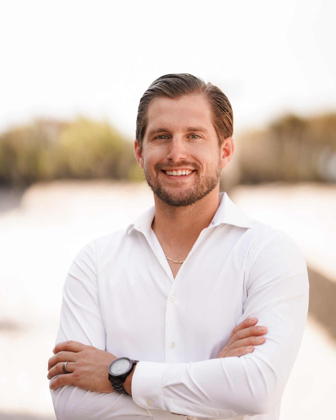 Paul D. Gibney smiling in a white shirt with his arms crossed outdoors.