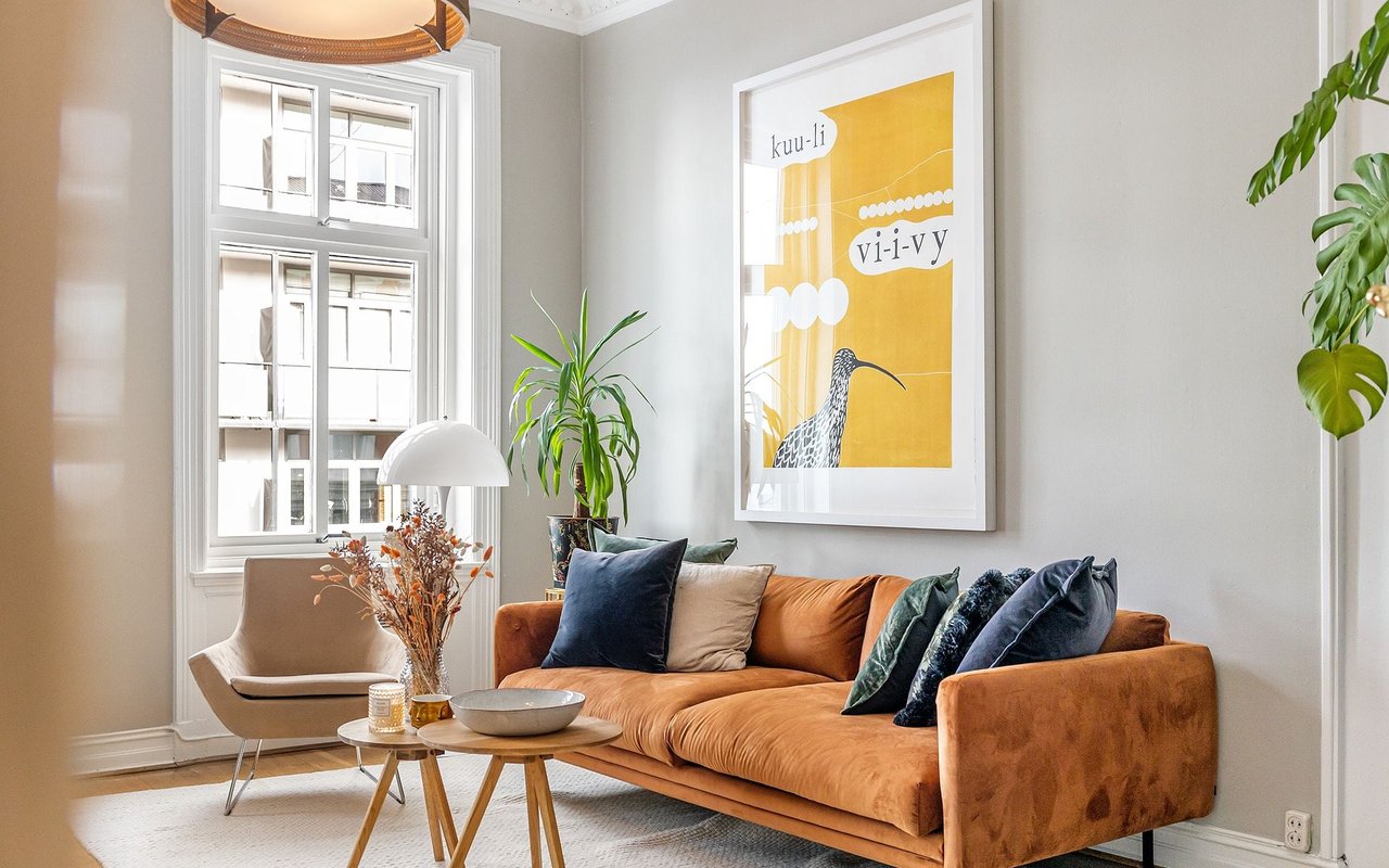 Living room with a rust-colored sofa, tall windows, and framed yellow artwork.