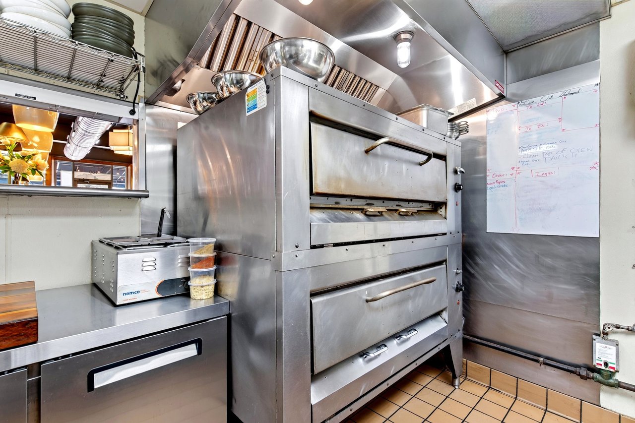 Restaurant kitchen with a large stainless-steel double-deck oven beneath a ventilation hood.