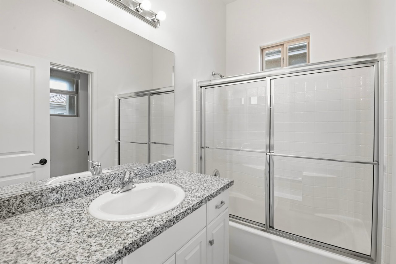 Bathroom with dual-sink granite vanity, framed mirror, and glass-enclosed tub-shower combo